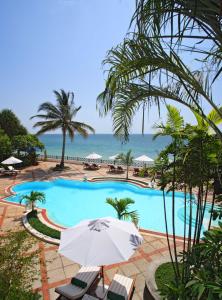 a swimming pool with an umbrella and the ocean at Zanzibar Serena Hotel in Zanzibar City