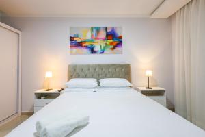 a white bedroom with a large bed and two lamps at Little Britain no centro de Pomerode in Pomerode