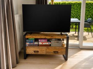 a flat screen tv on a wooden stand with a table at Veluwe Droom Chalet in Hoenderloo