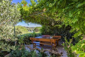 a wooden bench in a garden with trees and bushes at Apartments Petra - 100 m from the Beach in Kampor