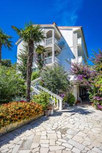 a white house with a palm tree and flowers at Apartments Petra - 100 m from the Beach in Kampor