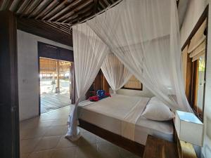 a bedroom with a bed with a mosquito net at Belar Reef Bungalows in Nembrala
