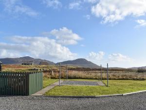 a park with a playground with a fence and mountains at Lochboisdale Cottage in Lochboisdale