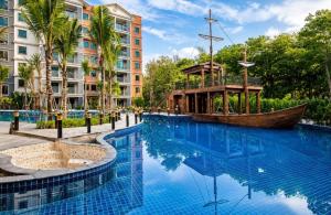 a large swimming pool with a wooden boat in front of a building at The Title Residencies Naiyang in Phuket