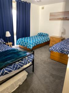 two beds in a room with blue curtains at Goolwa Retreat in Goolwa North