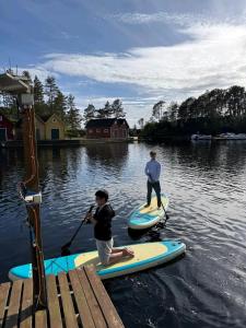 two people are on paddle boards on the water at Boat Included, Waterfront Villa, Near Bergen in Lindås