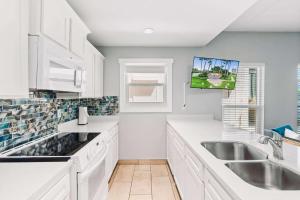 a kitchen with white cabinets and a tv on the wall at SPI Beach Condo - Just a block away to Paradise in South Padre Island