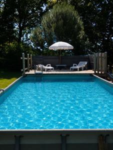 a large blue swimming pool with an umbrella and chairs at Gite "home" - piscine in Juvigny-le-Tertre