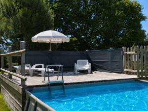 a deck with chairs and an umbrella next to a swimming pool at Gite "home" - piscine in Juvigny-le-Tertre