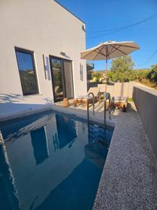 a swimming pool with an umbrella next to a house at Sage Villas in Plataria