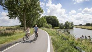 two people riding bikes on a road next to a river at B&B Het Doctershoes in Kinrooi