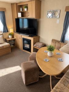 a living room with a table and a flat screen tv at Beachside 3 Bed Caravan with Deck & Outside Seating Mablethorpe in Mablethorpe