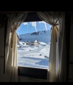 a window with a view of a house in the snow at Alojamiento FARAH in Caviahue