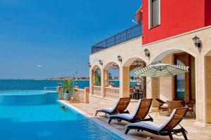 a pool with chairs and an umbrella next to a building at Apartament BEACH VIBES Nessebar in Nesebar