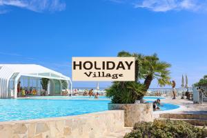 a holiday village sign in front of a swimming pool at Hotel Caraibi - Breakfast Until 11-00 and Dinner-Mirabilandia Partner in Milano Marittima