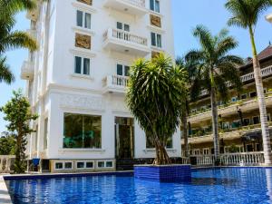 a building with palm trees in front of a swimming pool at Hotel HOÀNG THANH THỦY BÀ RỊA - VŨNG TÀU in Ho Coc