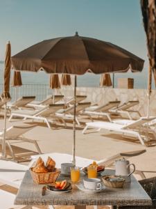 a table with breakfast food on the beach with an umbrella at Hotel de la Plage in Le Lavandou +49 photos