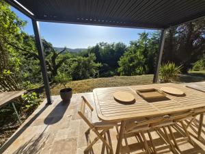 a wooden table and chairs on a deck with a view at Chez Nathan et Anaïs, Clim, piscine, pétanque, rivière in Vallon-Pont-dʼArc