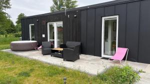 a black tiny house with pink chairs and a table at Domek nad Strugą przy stawach 10 km od Warszawy" Jacuzzi na zamówienie" in Halinow