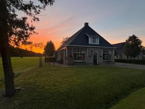 a house on a lawn with a sunset in the background at Recreatieappartement BoerdeRijlst - De Winkel in Sint Nicolaasga