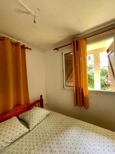 a bedroom with a bed and two windows with orange curtains at Corossole in Bouillante