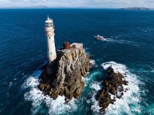 a lighthouse on a rock in the ocean with a boat at Marguerite's B&B in Skibbereen