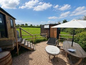 a patio with a table and an umbrella and a bench at Wiltshire Weavers Hut in Chippenham