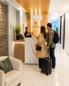 a man and a woman standing at a counter with luggage at Goya Hotel in Buenos Aires