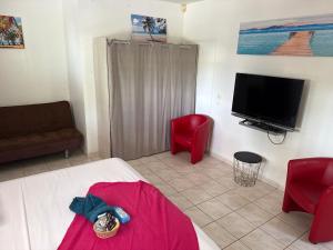 a room with a bed and two red chairs and a television at Le Pavillon Ananas in Gros-Morne