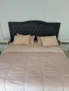 a large bed with a black headboard and pink pillows at Aura Residence in Comodoro Rivadavia