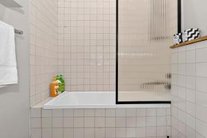 a white tiled bathroom with a tub and a shower at Ada Art Deco by Host Solutions Hutt St, Heritage in Adelaide +9 photos
