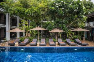 a swimming pool with lounge chairs and umbrellas next to a swimming pool at De Lanna Hotel in Chiang Mai