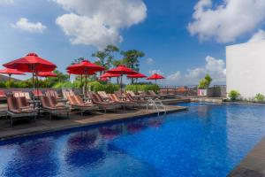 a swimming pool with chairs and red umbrellas at Sevn Legian in Legian