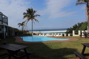 a swimming pool next to a beach with palm trees at Dumela Margate Flat No 2 in Margate