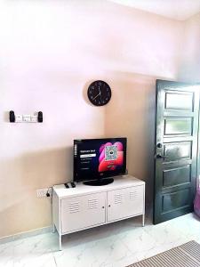 a clock on a wall with a tv on a cabinet at Adeeb Homestay in Tumpat