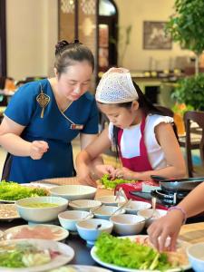 a woman and a girl preparing food on a table at Little Residence - A Boutique Hotel & Spa in Hoi An