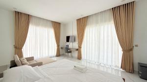 a bedroom with a white bed and a couch and windows at Soksan Nylen Hotel in Kampong Cham