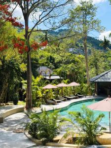 a pool at a resort with umbrellas and trees at Secret Cottages Chaweng Noi in Koh Samui