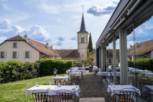 a courtyard with tables and a church with a clock tower at Auberge de Confignon in Geneva
