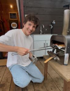 a man sitting on the floor in front of a pizza oven at ログハウス1棟貸し,持込み自由,サウナ,露天風呂にバーべキュウや薪割り,ソーメン流しに収穫体験が楽しめます in Kashima
