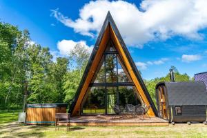 a cabin with a triangular roof with a deck and chairs at Frame Village in Žaugėdai