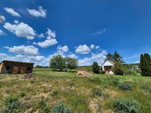 a field of grass with a barn and a blue sky at Alpaka Bakonya Kisház in Bakonya