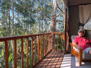 a man sitting in a chair on a porch at Kholiwe 1 - 4 sleeper glamping in a forest in Port Edward