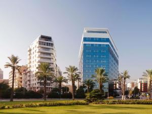 two tall buildings in a city with palm trees at Mövenpick Hotel Izmir in İzmir