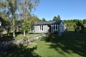 a small white house in a field with a yard at Rose Cottage in Puketapu