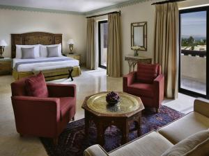 a hotel room with a bed and a couch and chairs at Mövenpick Resort & Spa Dead Sea in Sowayma
