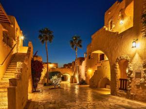an alley with palm trees and buildings at night at Mövenpick Resort & Spa Dead Sea in Sowayma