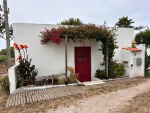 a small white house with a red door and flowers at Pé na Praia in Torres Vedras