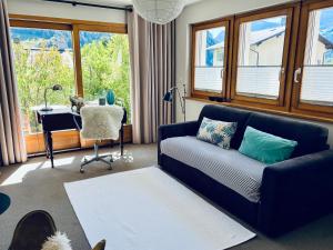 a living room with a couch and a desk and windows at Villa Fleurettes STUDIO in Le Châble