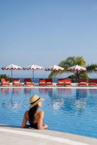 a woman in a hat sitting next to a swimming pool at Masana Algarve, Destination by Hyatt in Albufeira